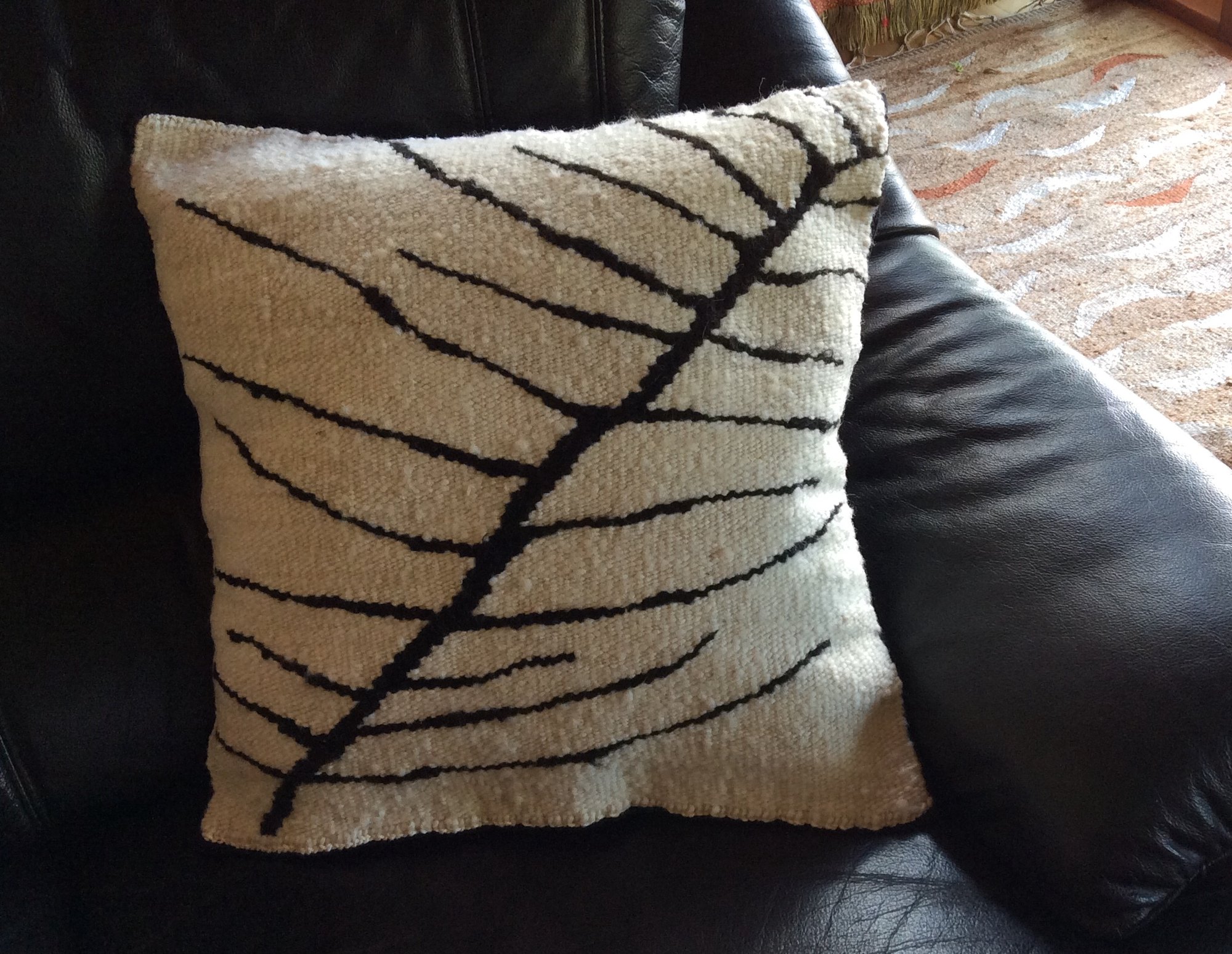 A tapestry cushion in natural cream wool with a bold black leaf, its veins reaching to the edges.
