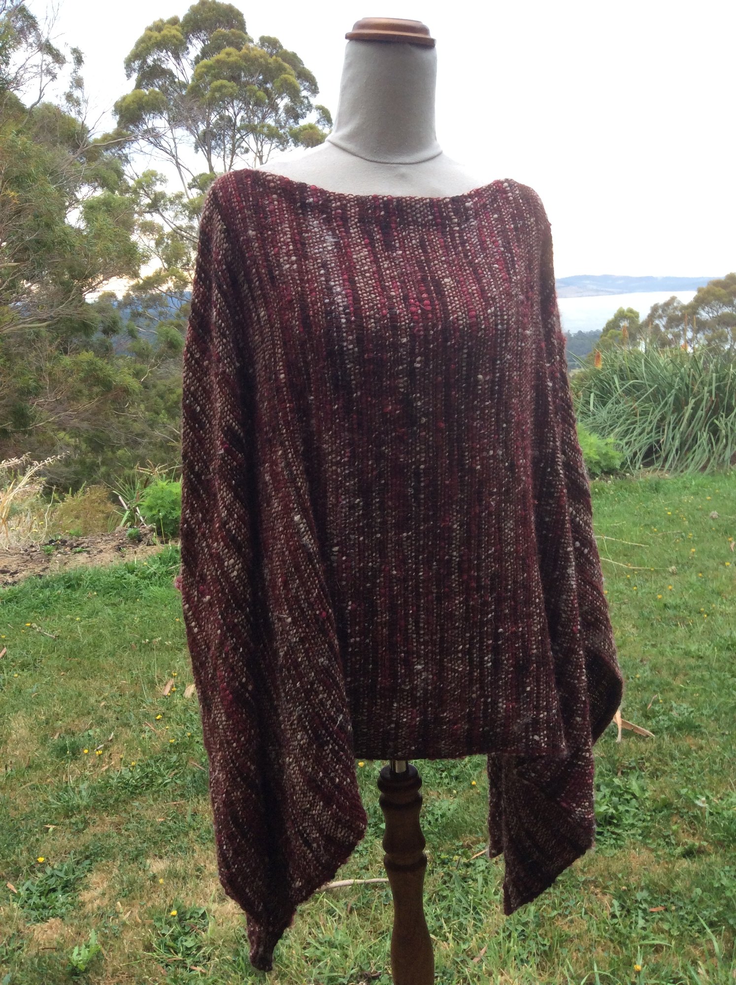 A loose poncho in mulberry, charcoal and flecks of oatmeal, woven from handspun yarn.