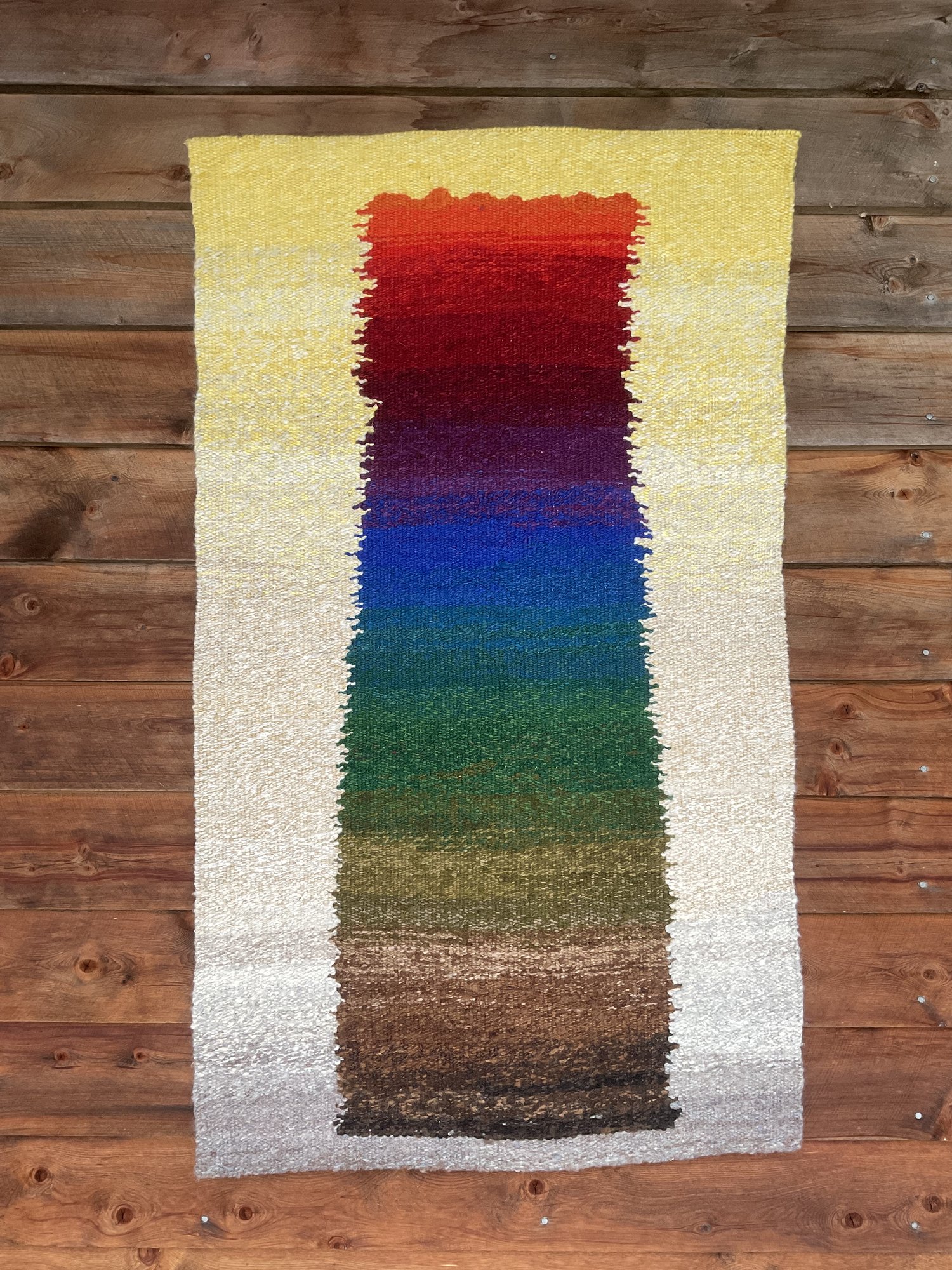 A tapestry that moves through the colours of the spectrum, from gold and red through blues and greens to earthy browns, set against cream.